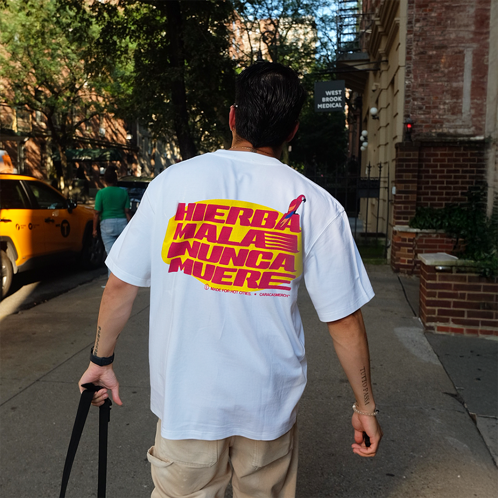 Modelo de espaldas llevando la camiseta blanca «Hierba Mala Nunca Muere» de Caracas Merch